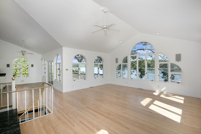 unfurnished living room with light wood finished floors, ceiling fan, a water view, and high vaulted ceiling
