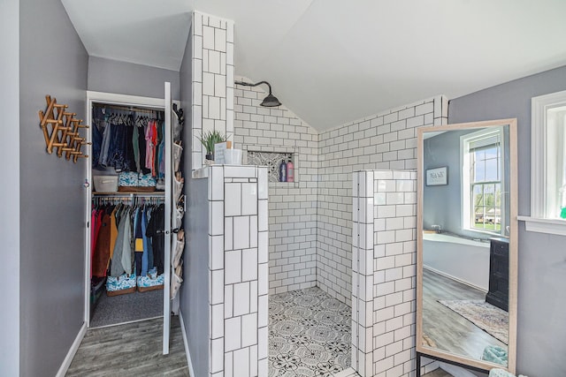 bathroom featuring wood finished floors, a walk in shower, baseboards, a spacious closet, and lofted ceiling