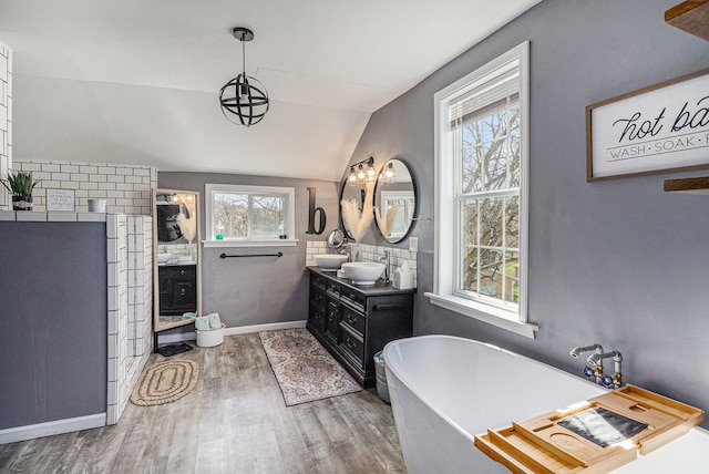 full bathroom with vanity, a freestanding tub, vaulted ceiling, baseboards, and wood finished floors