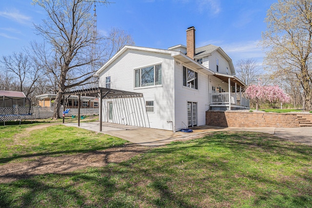 rear view of property with a trampoline, a chimney, a patio area, a lawn, and fence