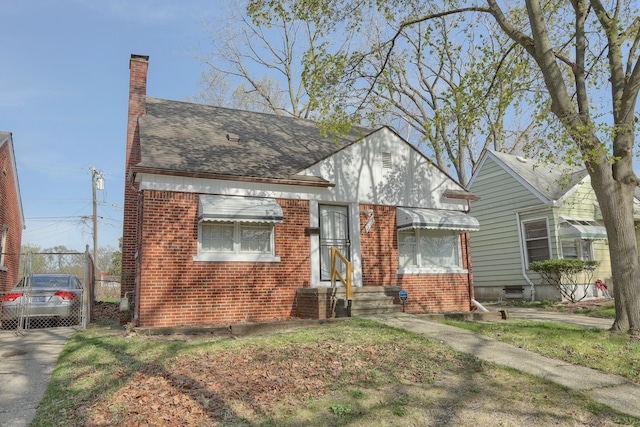 view of front of home featuring a chimney, brick siding, fence, roof with shingles, and concrete driveway