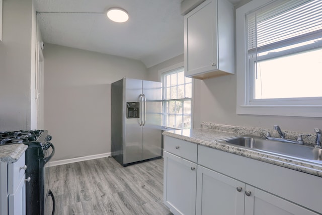 kitchen featuring black range with gas stovetop, stainless steel refrigerator with ice dispenser, light countertops, and light wood finished floors