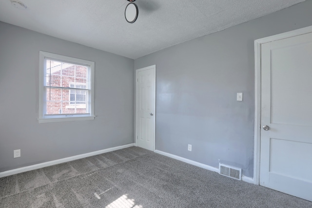 carpeted empty room with baseboards, visible vents, and a textured ceiling