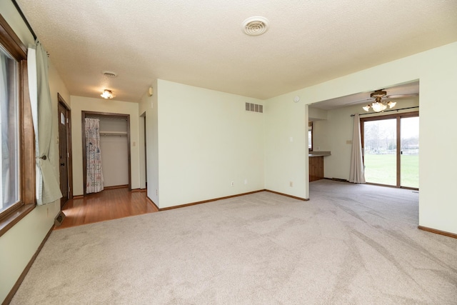 carpeted spare room with baseboards, visible vents, ceiling fan, and a textured ceiling