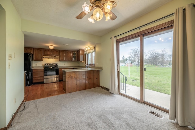 kitchen with stainless steel range with electric stovetop, under cabinet range hood, visible vents, carpet, and freestanding refrigerator