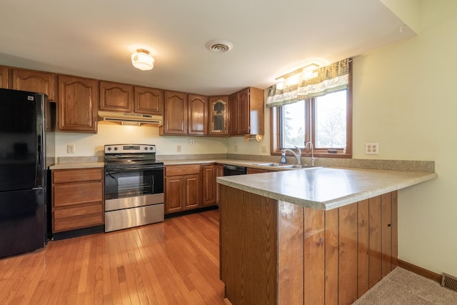 kitchen with a sink, under cabinet range hood, brown cabinetry, black appliances, and a peninsula