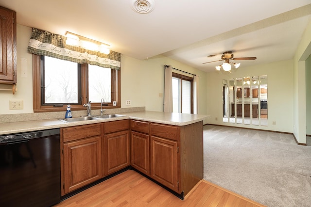 kitchen with black dishwasher, light countertops, brown cabinets, a sink, and a peninsula