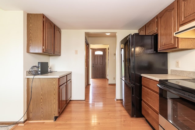 kitchen with light wood finished floors, under cabinet range hood, range with electric cooktop, brown cabinetry, and light countertops