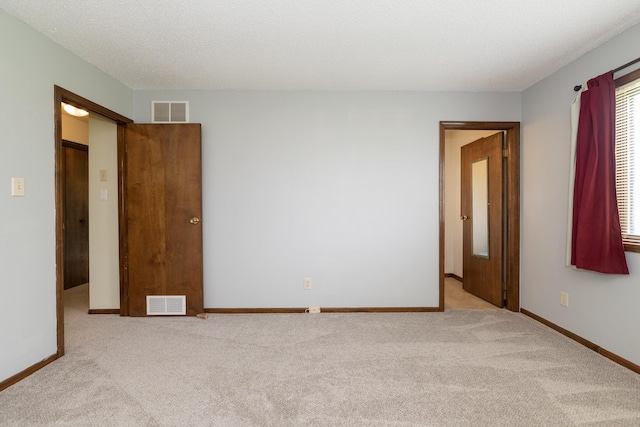 empty room featuring a textured ceiling, visible vents, carpet floors, and baseboards
