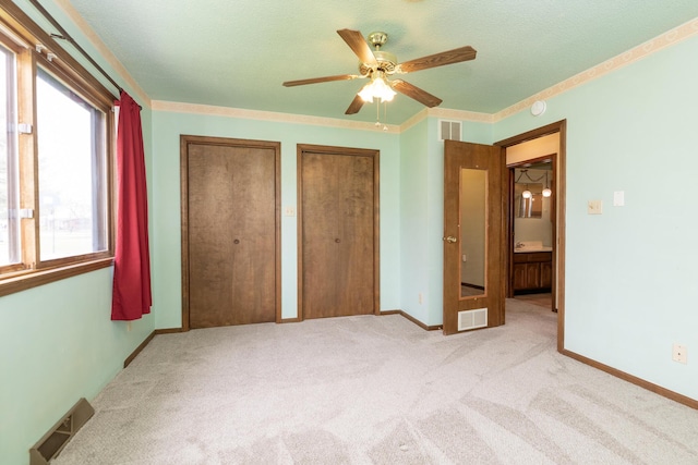 unfurnished bedroom featuring visible vents, two closets, and light carpet