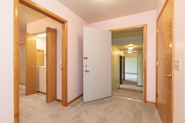 hallway featuring baseboards, washer / clothes dryer, and light colored carpet