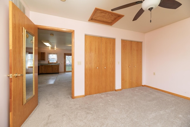 unfurnished bedroom with multiple closets, baseboards, a ceiling fan, and light carpet