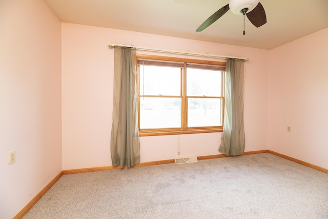 carpeted empty room featuring visible vents, a ceiling fan, and baseboards