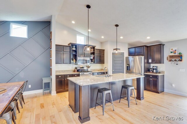 kitchen featuring appliances with stainless steel finishes, hanging light fixtures, a sink, light wood-style floors, and a breakfast bar