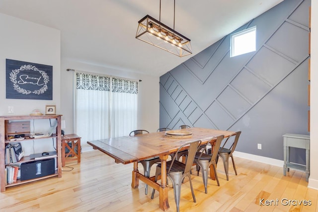 dining space with vaulted ceiling, baseboards, a decorative wall, and light wood-style flooring