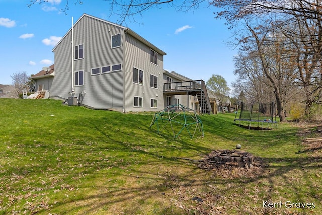 rear view of property featuring a lawn, a deck, central AC unit, and a trampoline