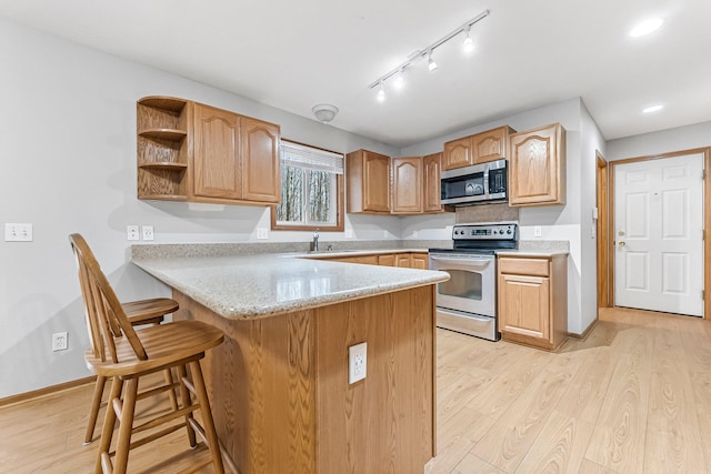 kitchen featuring light wood-style flooring, stainless steel appliances, open shelves, a sink, and a peninsula
