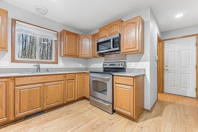 kitchen with a sink, light wood-style flooring, stainless steel appliances, and visible vents