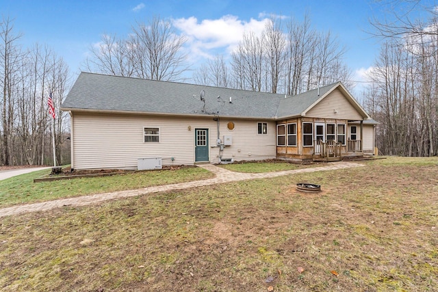 rear view of property featuring a sunroom, a yard, a fire pit, and roof with shingles