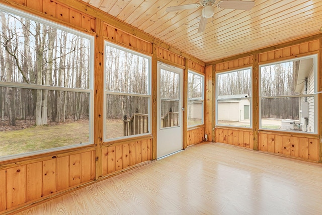 unfurnished sunroom with wood walls, wood finished floors, and ceiling fan