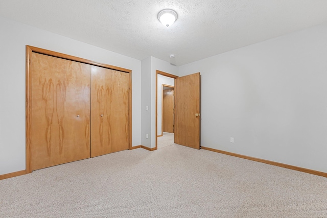 unfurnished bedroom with light colored carpet, a closet, a textured ceiling, and baseboards