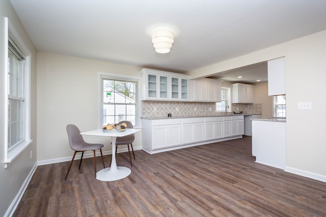 kitchen featuring white cabinets, glass insert cabinets, dark wood-style floors, baseboards, and backsplash