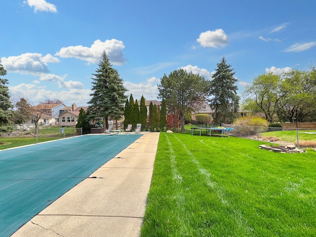 community pool with a lawn, a trampoline, and fence