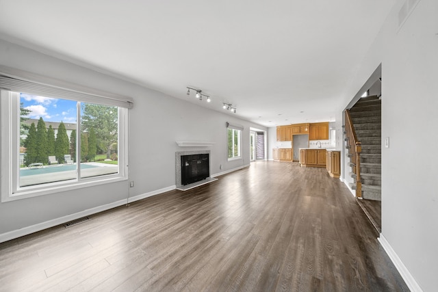 unfurnished living room with visible vents, plenty of natural light, dark wood-type flooring, and a glass covered fireplace