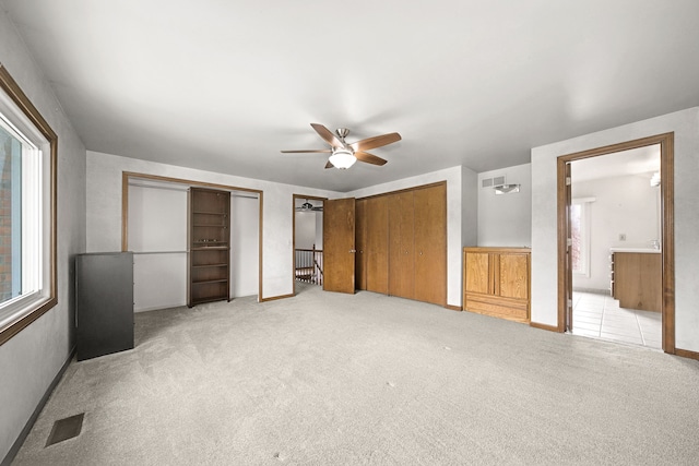 unfurnished bedroom featuring light colored carpet, visible vents, multiple closets, and multiple windows