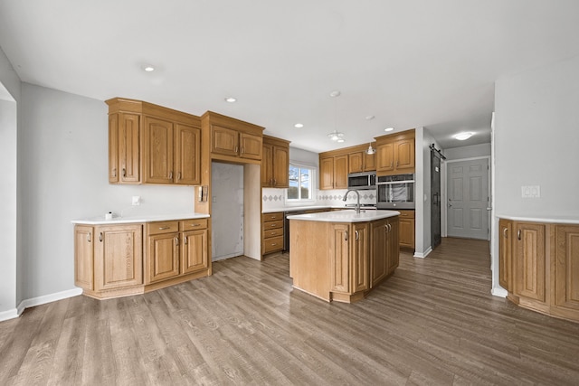 kitchen with an island with sink, wood finished floors, appliances with stainless steel finishes, and light countertops