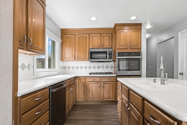 kitchen with appliances with stainless steel finishes, decorative backsplash, dark wood finished floors, and a sink