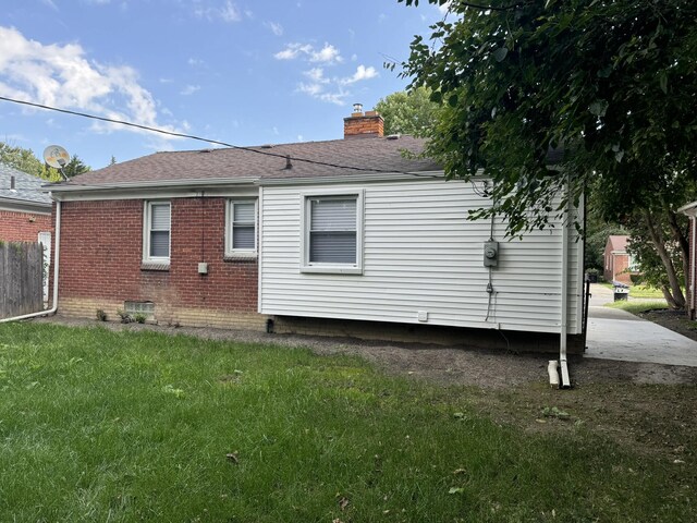 back of property featuring a chimney, roof with shingles, fence, a yard, and brick siding