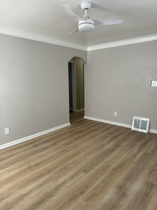 unfurnished room with arched walkways, wood finished floors, ceiling fan, baseboards, and visible vents