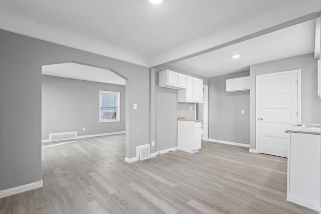 unfurnished living room with arched walkways, light wood finished floors, a sink, baseboards, and visible vents