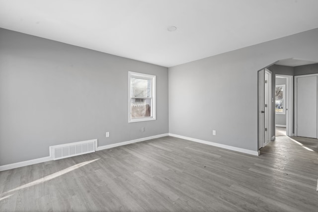 empty room with a wealth of natural light, visible vents, wood finished floors, and arched walkways