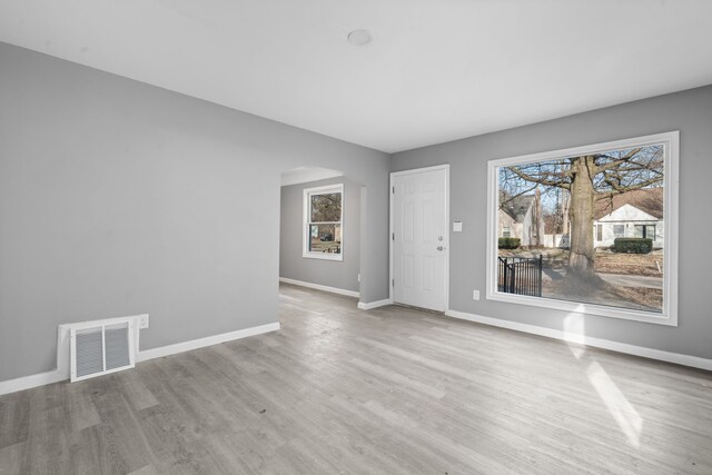 unfurnished room with arched walkways, visible vents, wood finished floors, and plenty of natural light