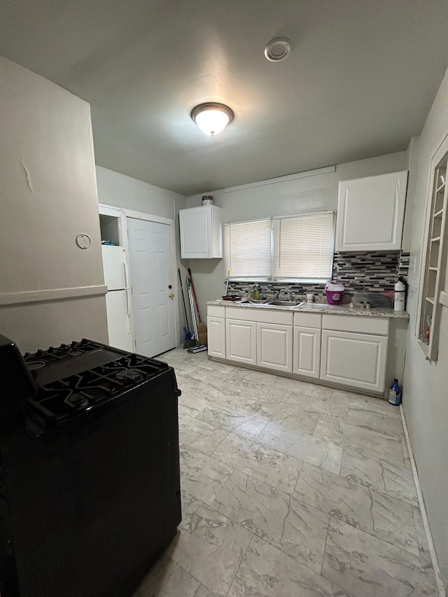 kitchen featuring decorative backsplash, marble finish floor, white cabinets, baseboards, and black gas range
