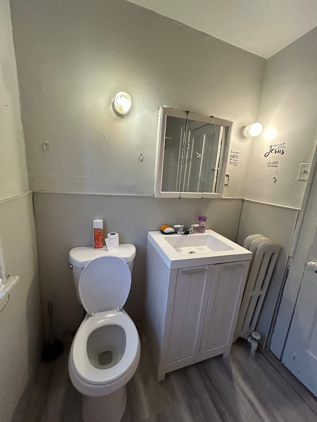 bathroom with radiator heating unit, wood finished floors, toilet, and vanity