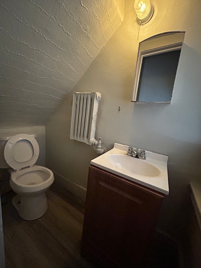 half bath with vanity, lofted ceiling, toilet, baseboards, and wood finished floors