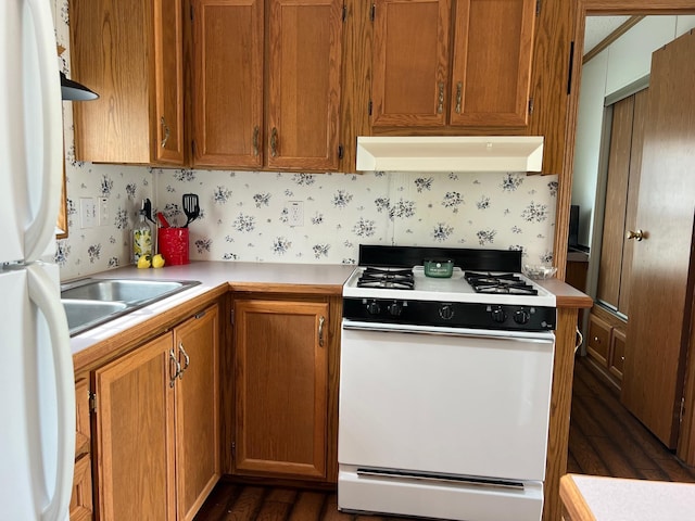 kitchen with white appliances, under cabinet range hood, light countertops, brown cabinets, and dark wood-style flooring