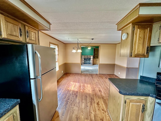 1088 Kern Rd, Fowlerville, MI 48836 - kitchen with freestanding refrigerator, a stone fireplace, light wood finished floors, dark countertops, and a textured ceiling