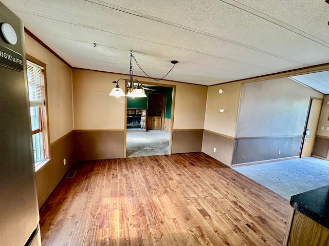 1088 Kern Rd, Fowlerville, MI 48836 - empty room with wood finished floors, a textured ceiling, crown molding, a fireplace, and a wainscoted wall