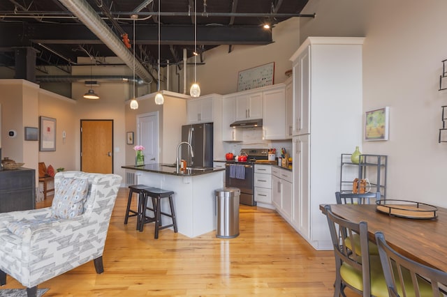 kitchen featuring appliances with stainless steel finishes, under cabinet range hood, dark countertops, white cabinetry, and a high ceiling