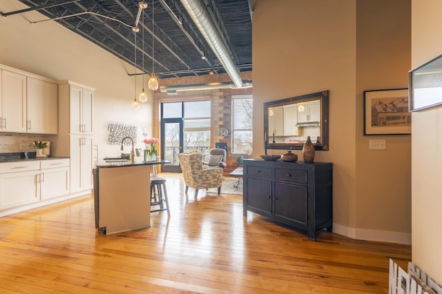 kitchen featuring a towering ceiling, dark countertops, light wood-type flooring, and white cabinets