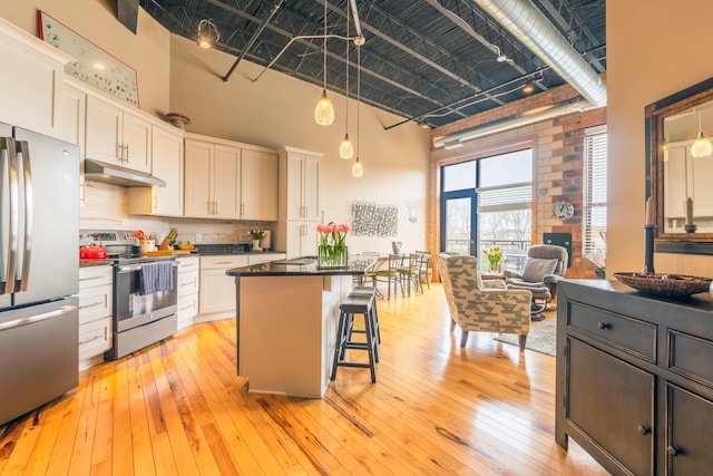kitchen featuring white cabinets, dark countertops, stainless steel appliances, under cabinet range hood, and a high ceiling