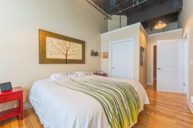 bedroom with a towering ceiling, hardwood / wood-style floors, and baseboards