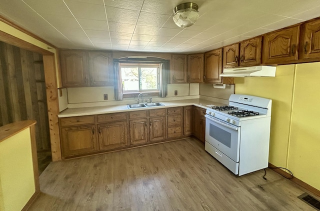 kitchen with a sink, white gas range, visible vents, under cabinet range hood, and brown cabinetry