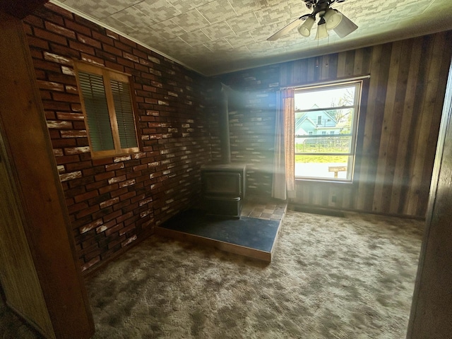 empty room with a wood stove, carpet flooring, brick wall, ceiling fan, and an ornate ceiling