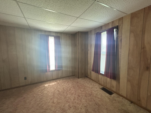 empty room featuring a wealth of natural light, visible vents, a drop ceiling, and carpet floors