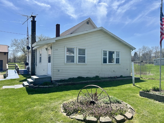 back of house featuring a chimney, fence, and a lawn